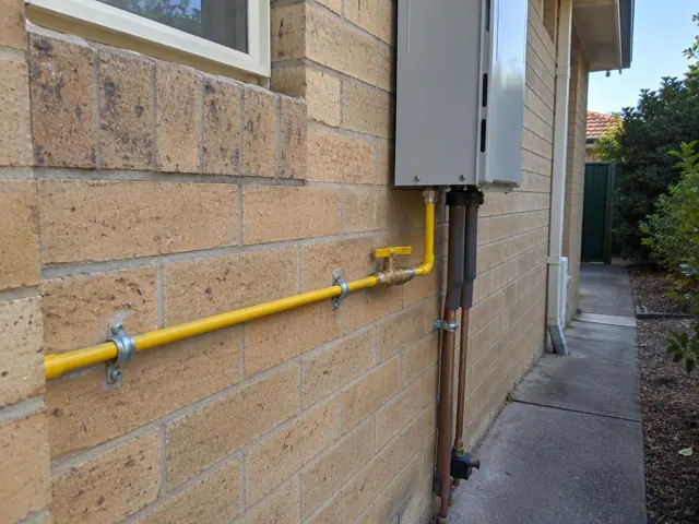 Yellow gas pipe and fittings on a brick exterior wall beside a home in Beverly Hills