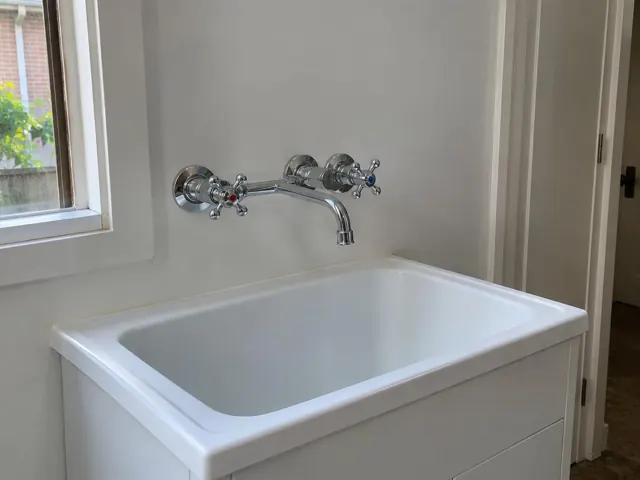 Chrome wall-mounted laundry tap above a white trough with dry sink and bench in a light room in Penshurst